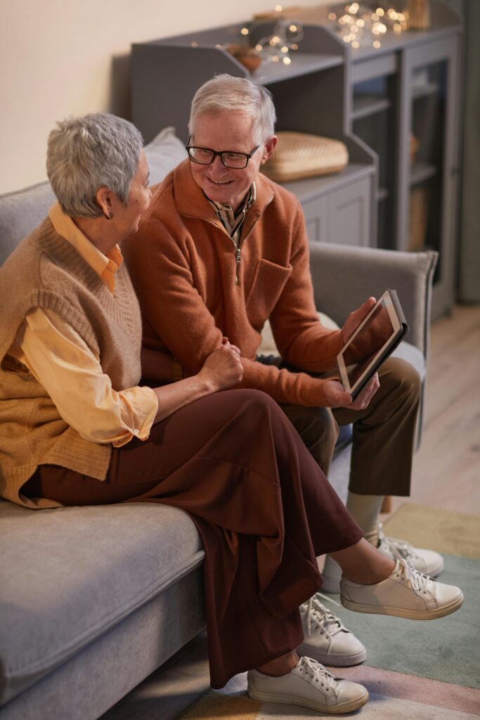 A happy senior couple sitting on a sofa engaging with a tablet indoors.